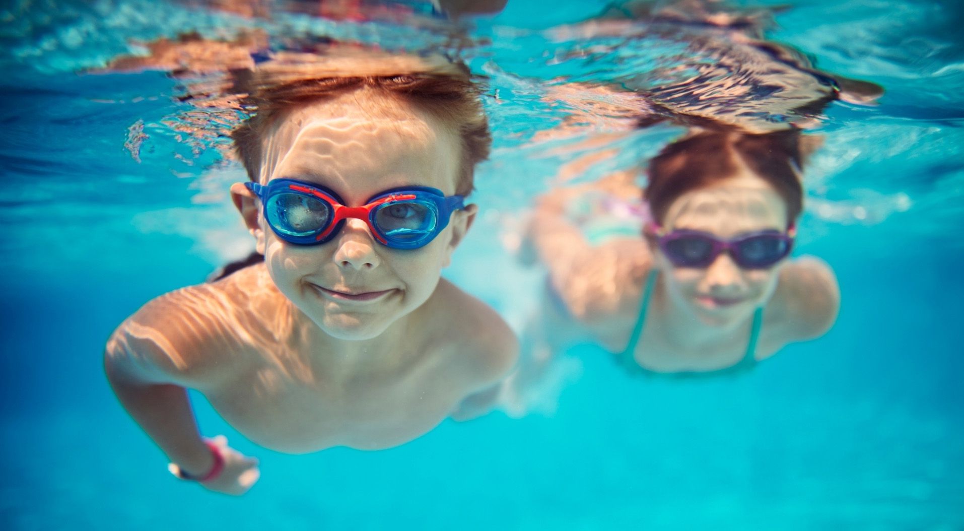 Two kids swimming underwater in pool with goggles
